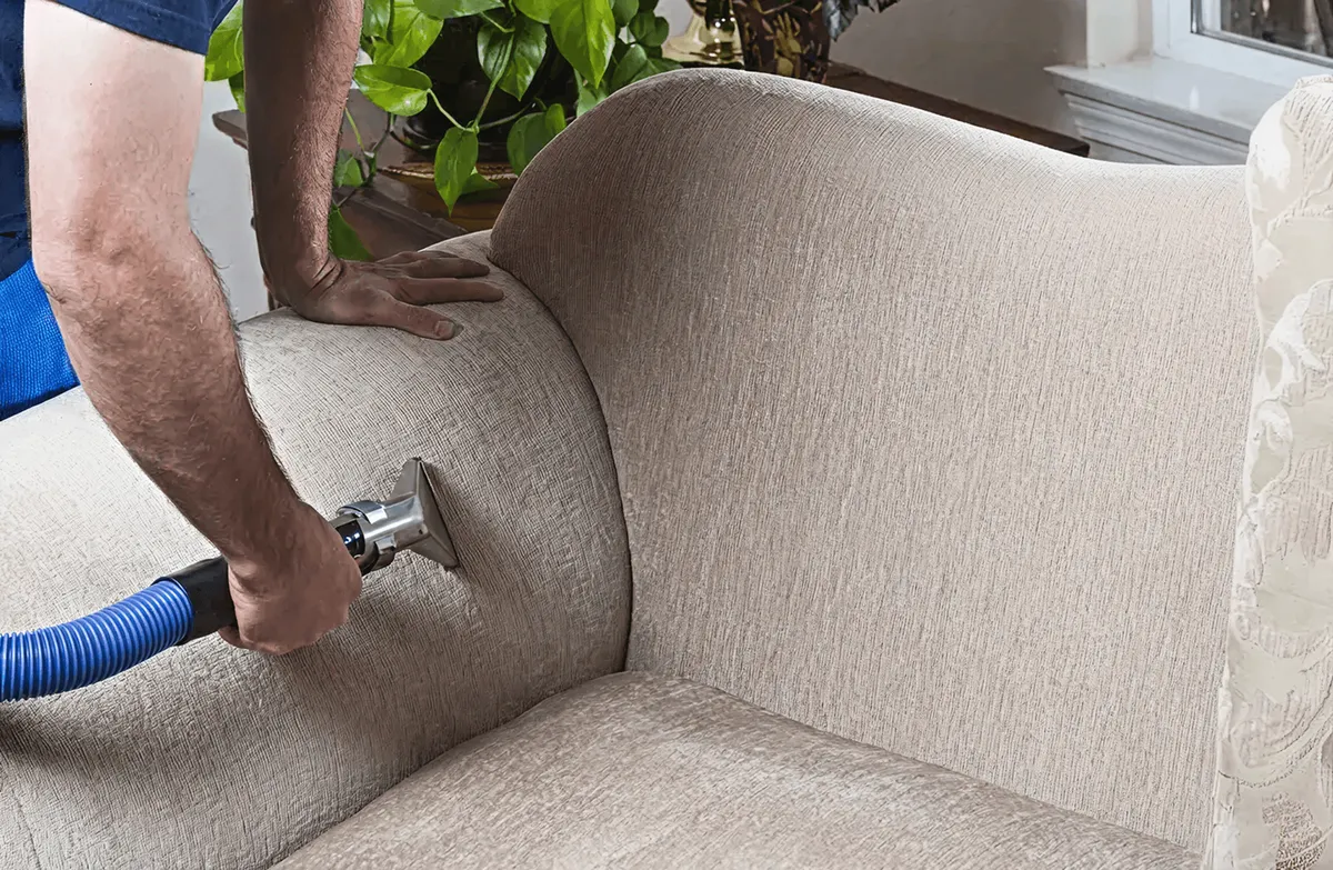 Professional upholstery cleaner deep-cleaning a fabric sofa with a handheld extraction tool and hose, Long Beach, CA.